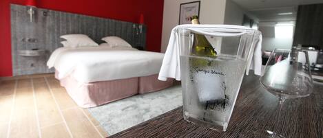 A hotel room with a bed, a table with a bottle of champagne and a glass, and a red wall.