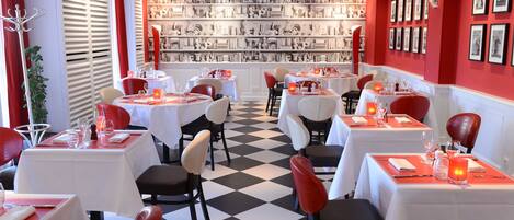 Un restaurante con mesas dispuestas para comer, un fondo con pared decorada y cortinas rojas.