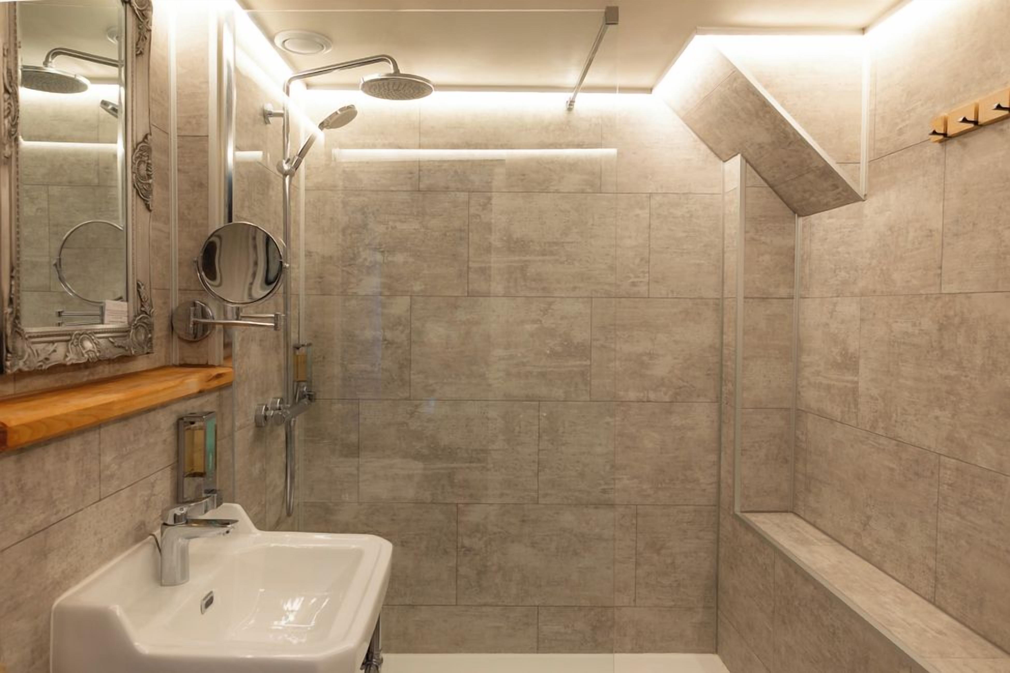 A modern bathroom with a sink, mirror, shower, and a bench.