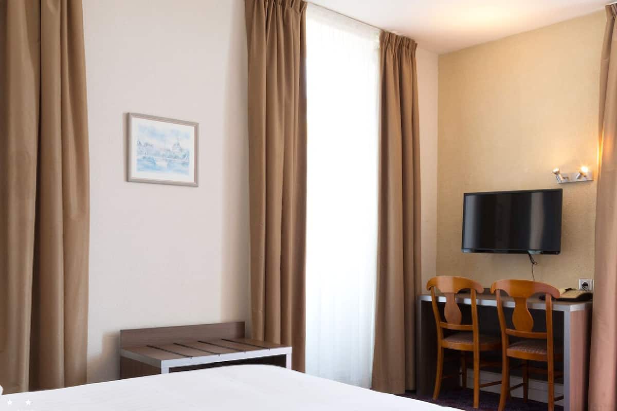 A hotel room with a bed, a desk with two chairs, a television mounted on the wall, and a framed picture on the wall.