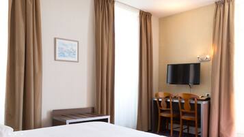 A hotel room with a bed, a desk with two chairs, a television mounted on the wall, and a framed picture on the wall.