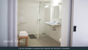Un baño moderno con ducha, lavamanos e inodoro. Se observa un perchero y un taburete de madera. Las paredes y el suelo están cubiertos de azulejos.