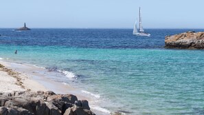 Un paysage côtier avec une eau turquoise et limpide, une plage de sable et des affleurements rocheux.