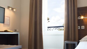 Quarto de hotel com cama, escrivaninha com telefone e janela com cortinas.