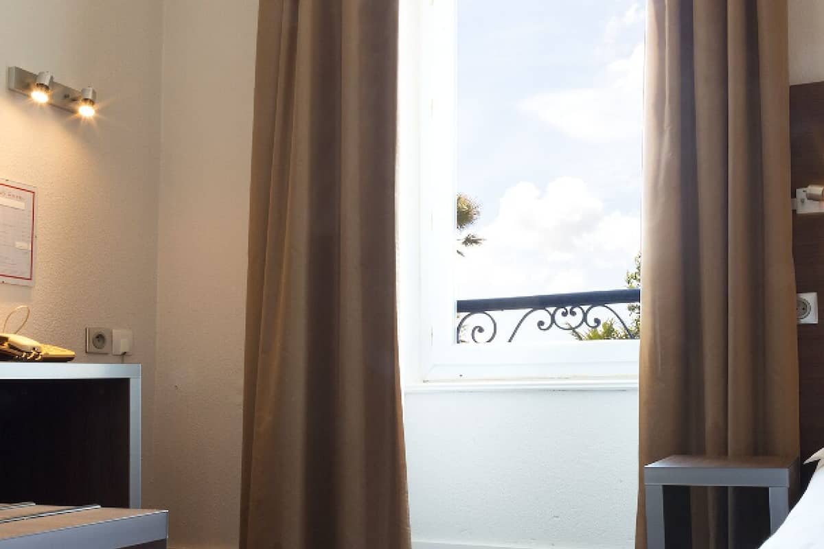 A hotel room with a bed, a desk with a telephone, and a window with curtains.