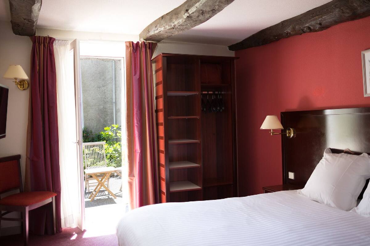 A hotel room with a bed, a wooden wardrobe, a desk, a chair, a television, and a balcony with a chair.