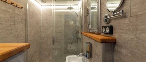 Un baño moderno con ducha de vidrio, lavamanos blanco y encimera de madera.