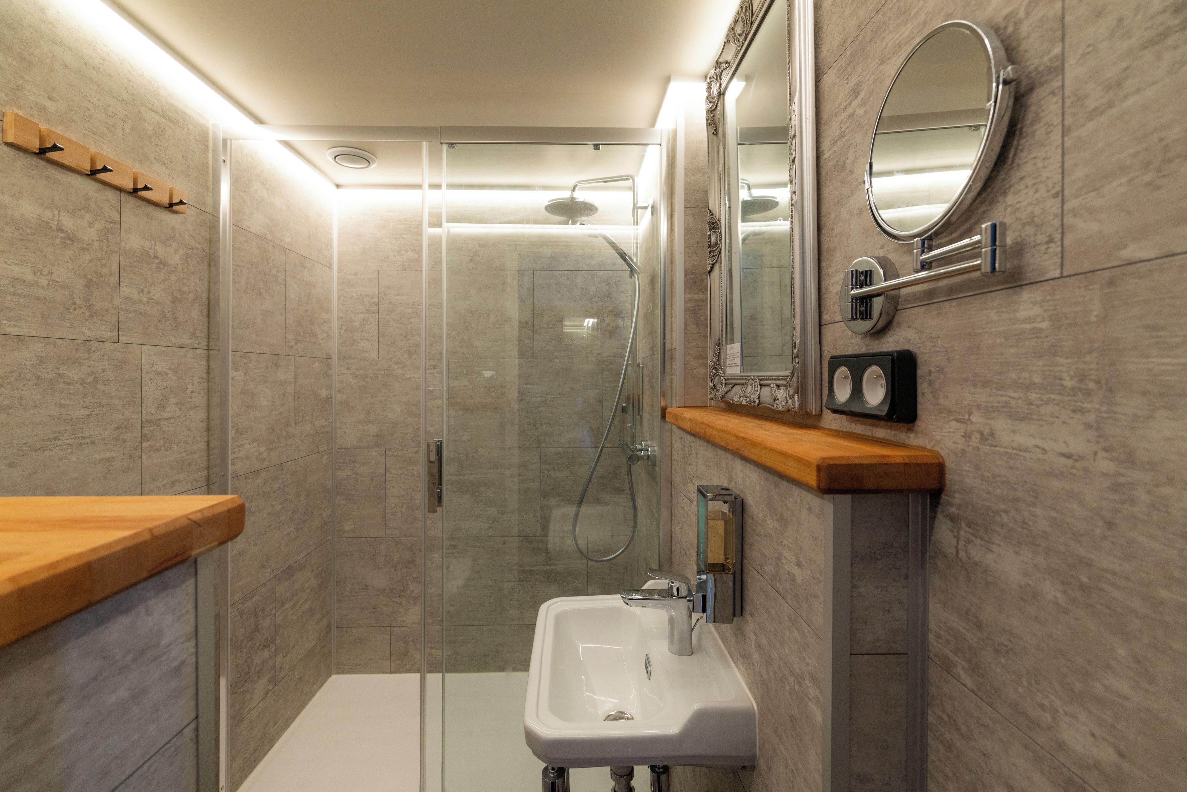 Un bagno moderno con cabina doccia in vetro, lavabo bianco e mobile vanitario in legno.