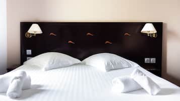 Cama bem arrumada com roupa de cama e toalhas brancas, cabeceira escura com duas luminárias fixadas na parede, e design de parede simples.