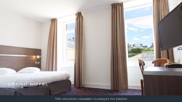 Habitación de hotel con una cama grande, un escritorio y un televisor. La habitación tiene ventanas amplias con cortinas y vistas al exterior.