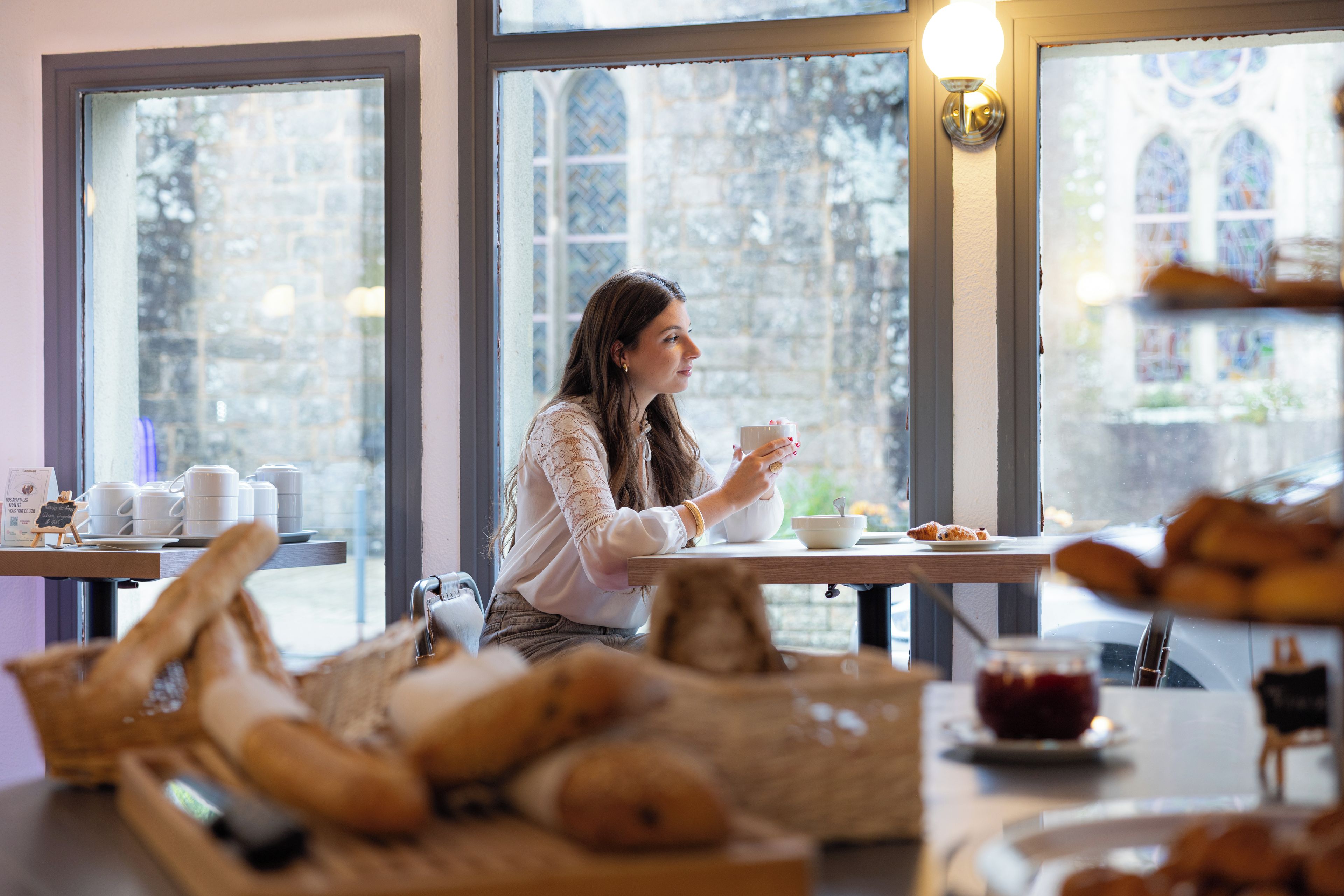Una persona sentada a una mesa con una taza, pasteles y un bol.
