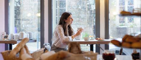 A person seated at a table with a cup, pastries, and a bowl.