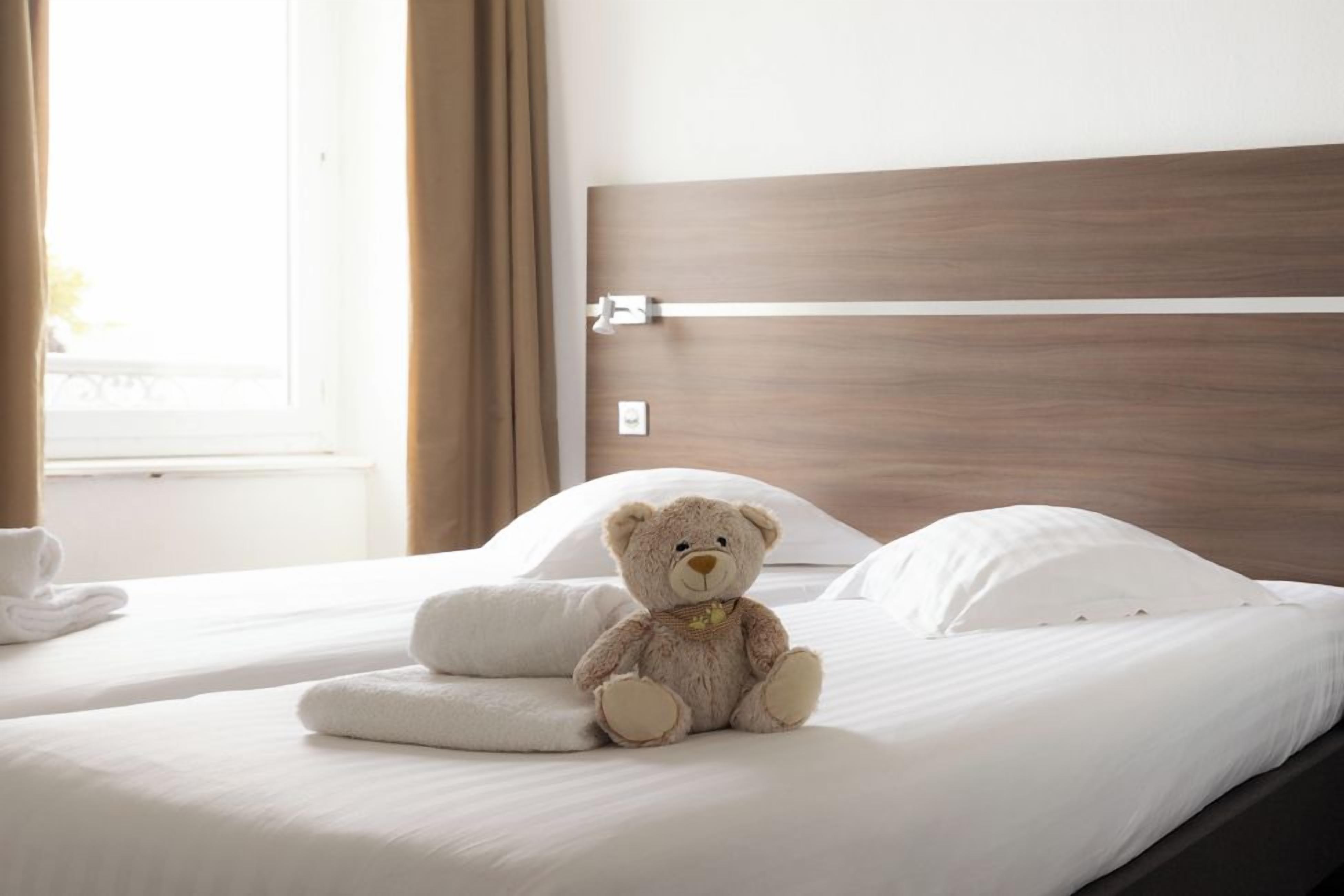 Una cama con un osito de peluche, almohadas blancas y un cabecero de madera.