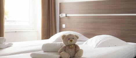 Una cama con un osito de peluche, almohadas blancas y un cabecero de madera.