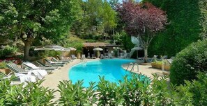 A swimming pool surrounded by lounge chairs and umbrellas, with trees and a small building in the background. - Villa Borghese, The Originals Relais (Gréoux-les-Bains)