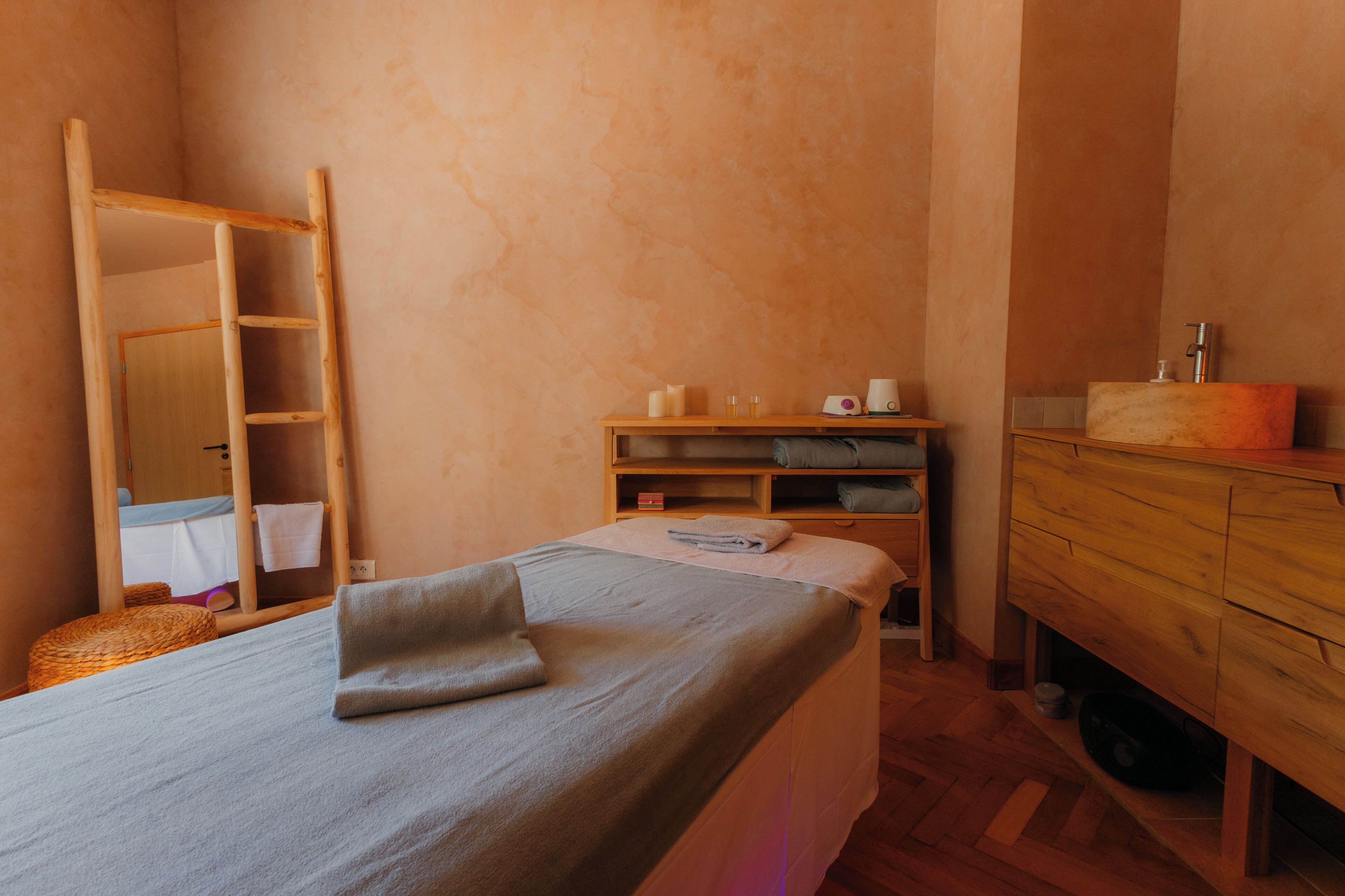 Una cama individual con una almohada, un aparador de madera, un espejo y una estantería con objetos.