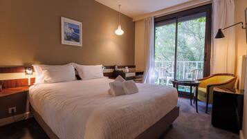 A hotel room with a large bed, a desk, a chair, and a window with a view of trees.