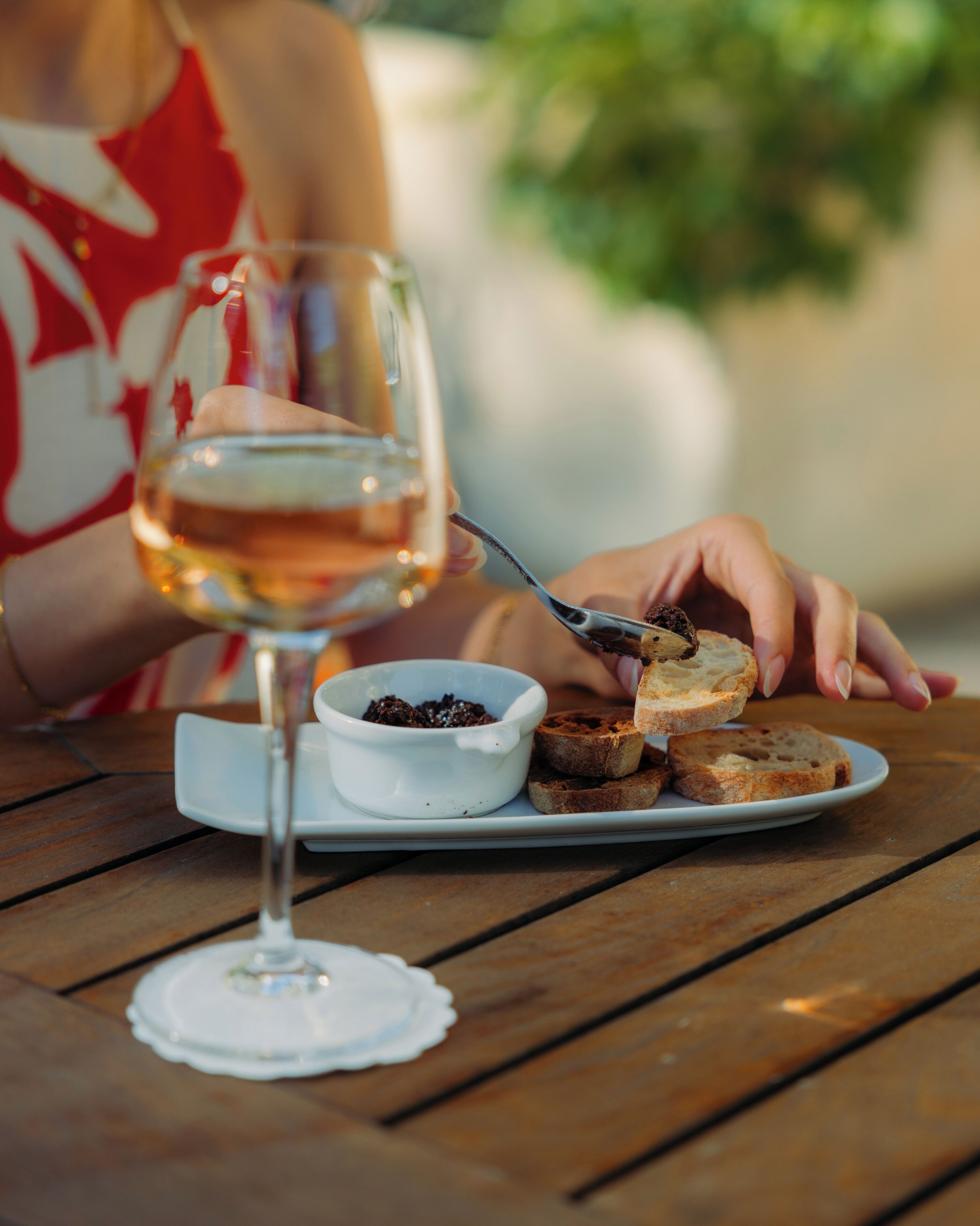 A dining table with a plate of bread and a small bowl of spread, a glass of wine, and a white napkin.