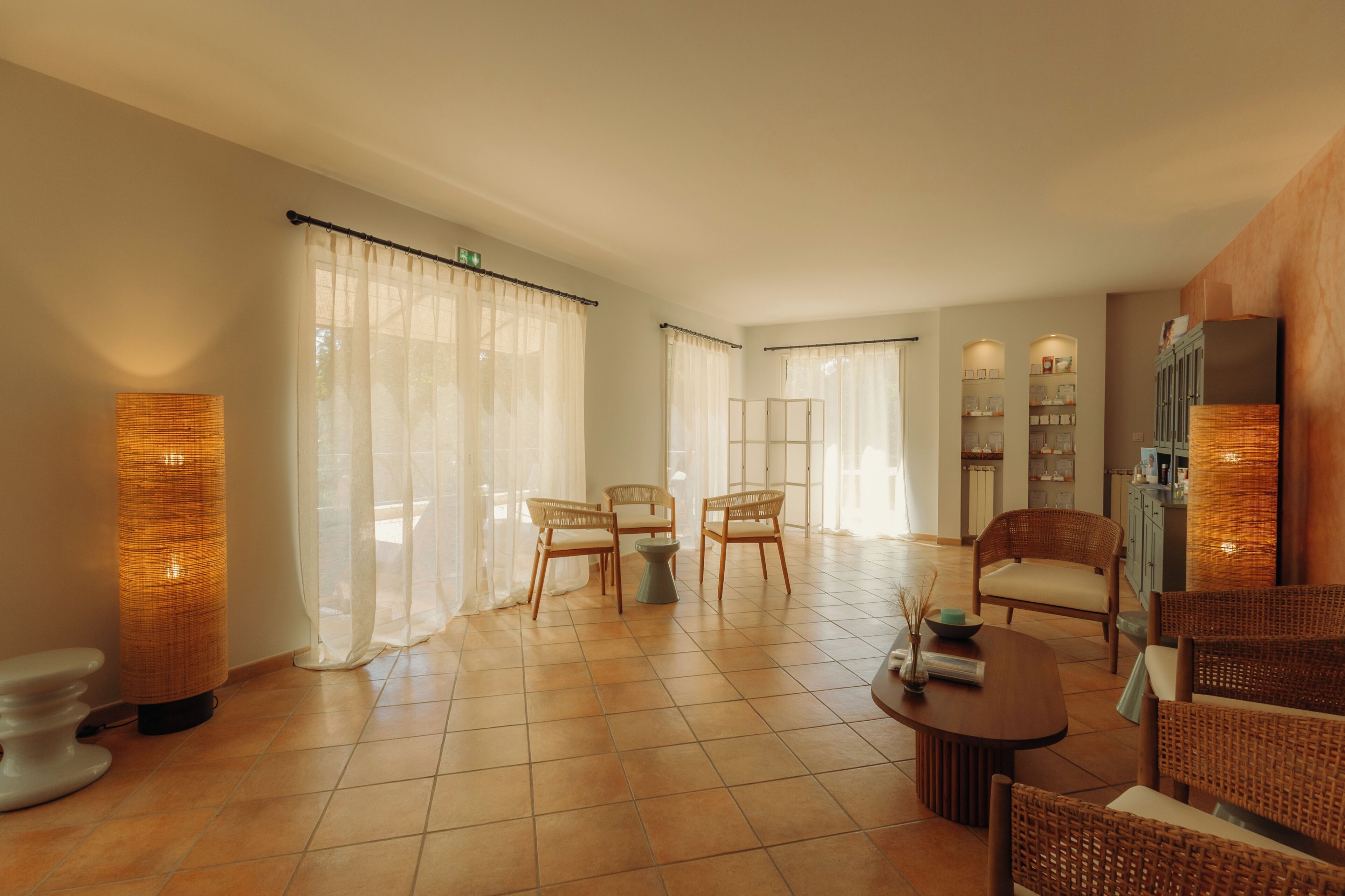 A hotel room with a dining area, two wicker chairs, a round table, and a cabinet with shelves.
