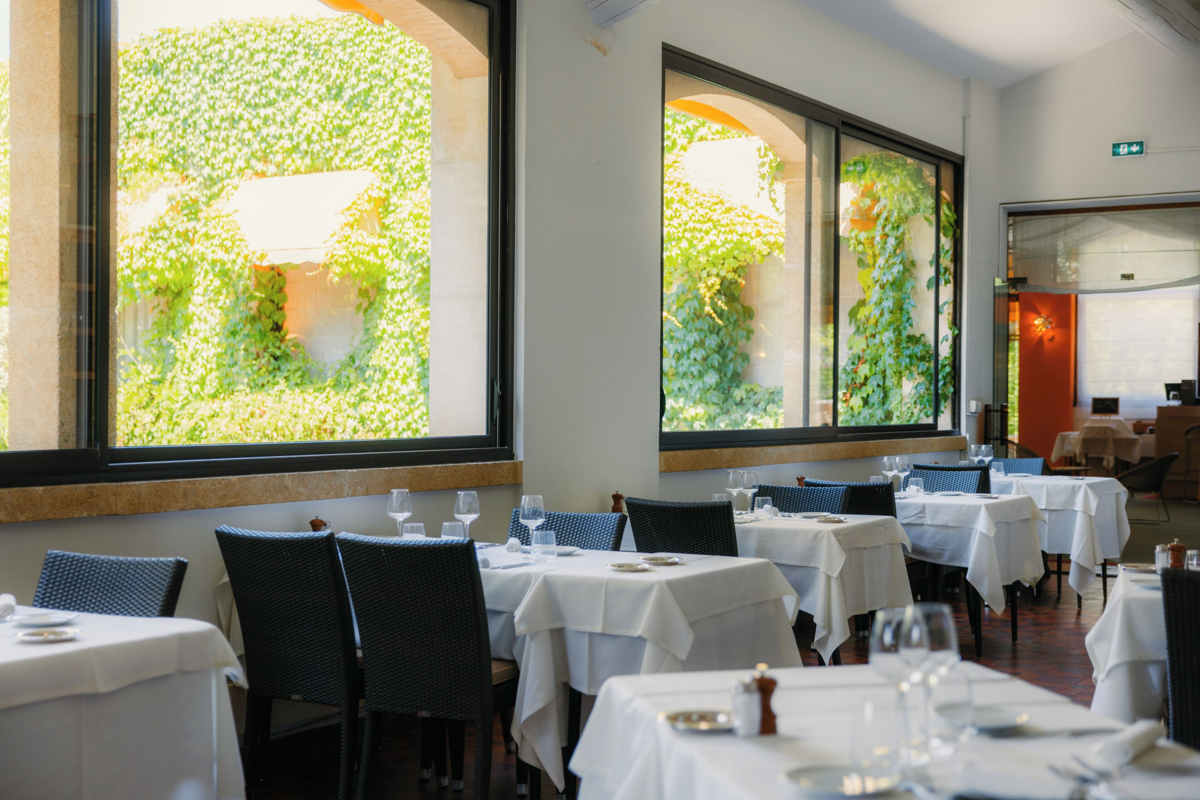 A restaurant interior with multiple tables, chairs, and large windows with greenery views.