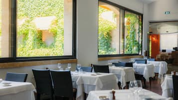 A restaurant interior with multiple tables, chairs, and large windows with greenery views.