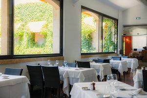 Interior de restaurante con varias mesas, sillas y ventanas amplias que dan a vistas de follaje.