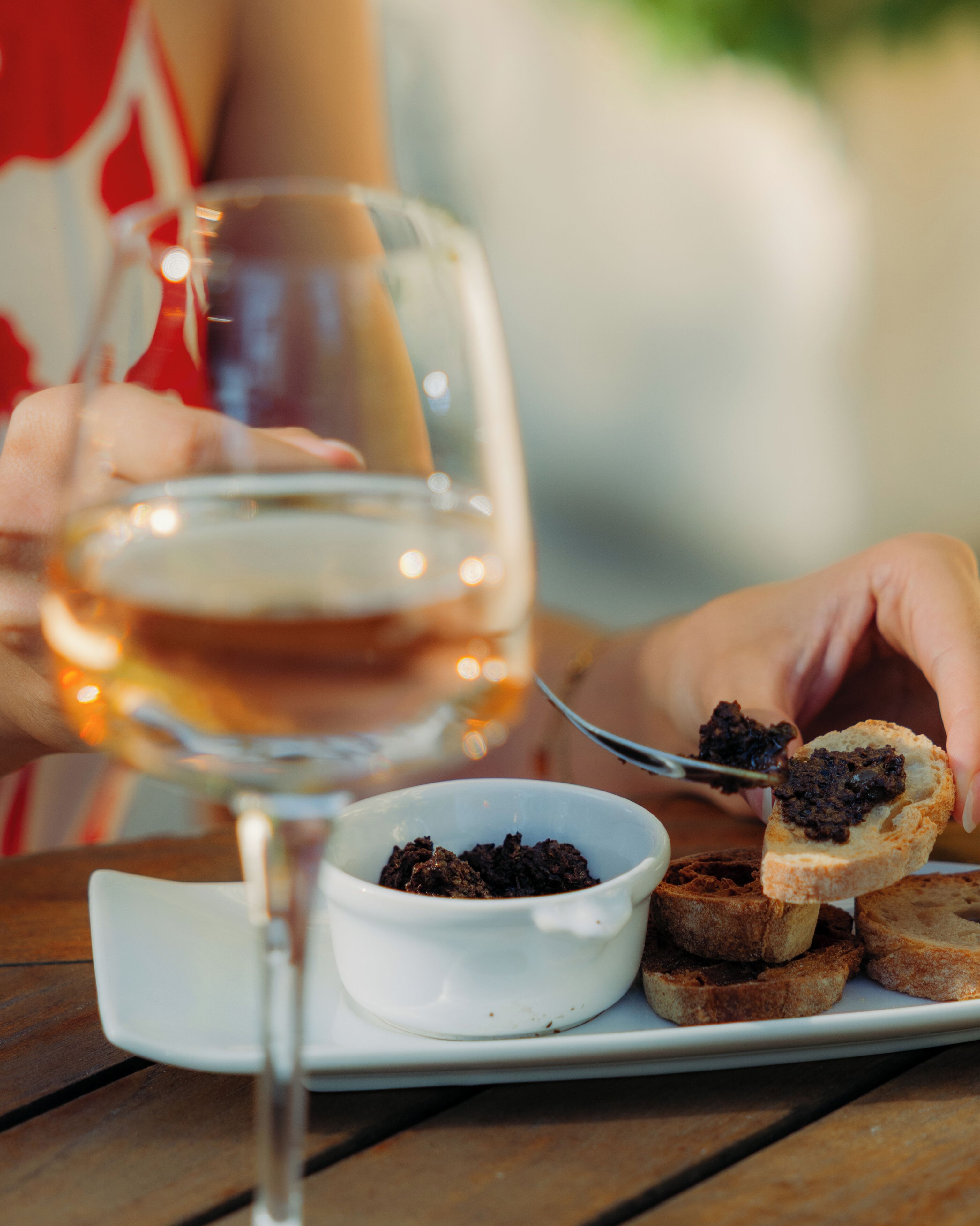A dining table with a glass of white wine, a small bowl of dark spread, and toasted bread.