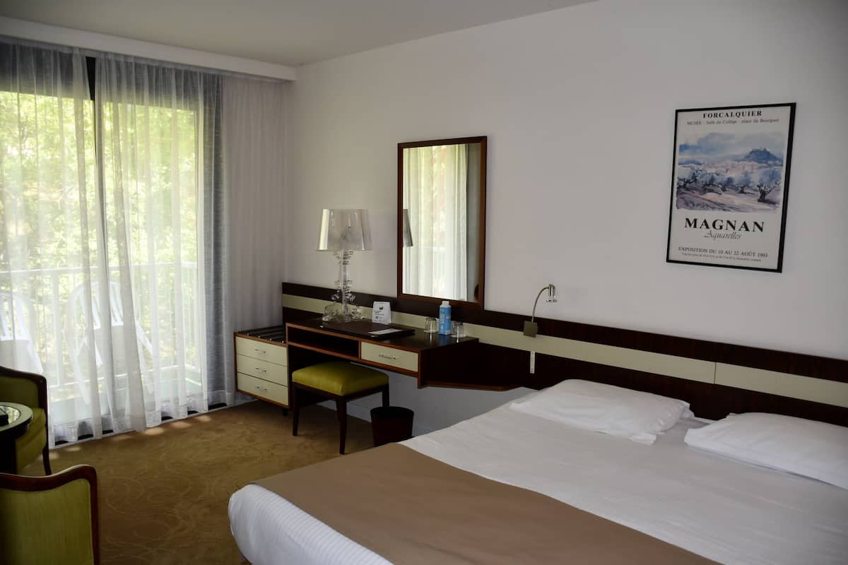A hotel room with a bed, a desk, a chair, a lamp, and a poster on the wall.