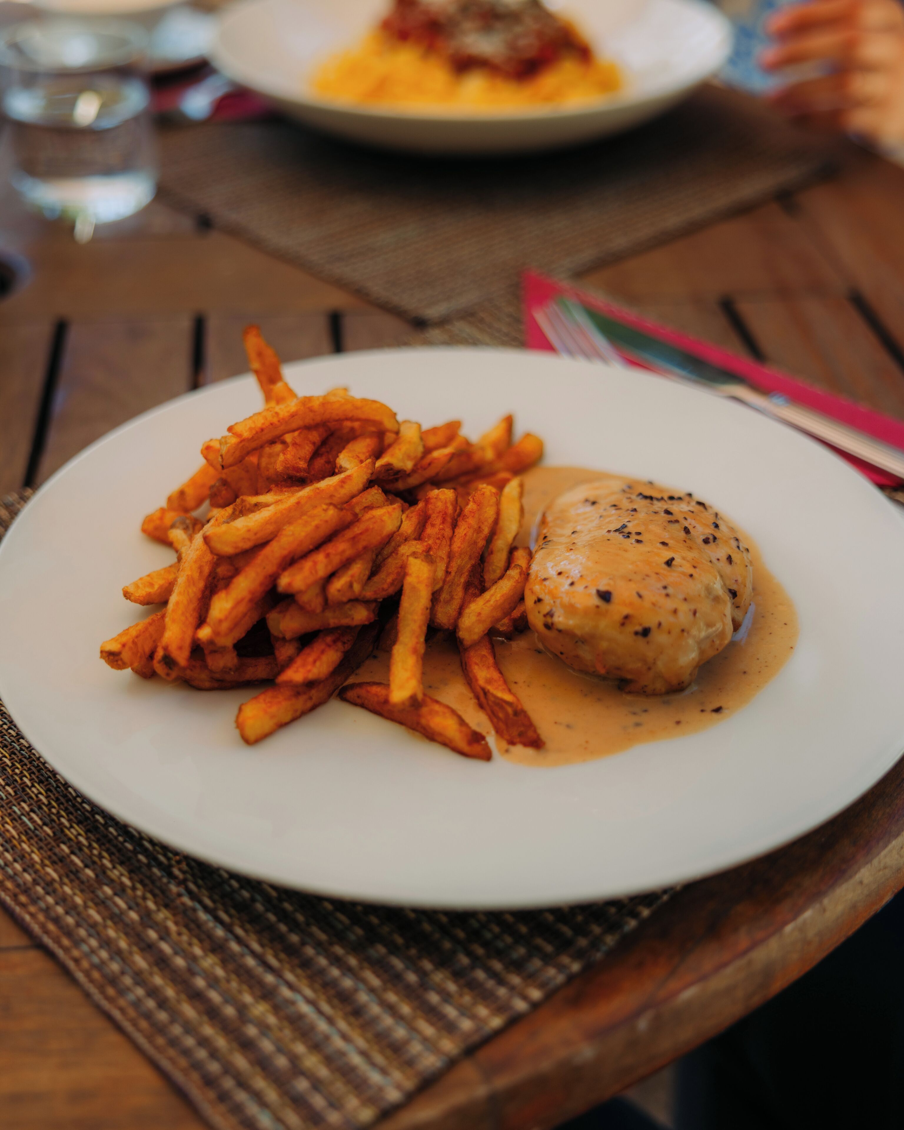 A plate of food with fries and a meat dish, possibly chicken, on a wooden table.