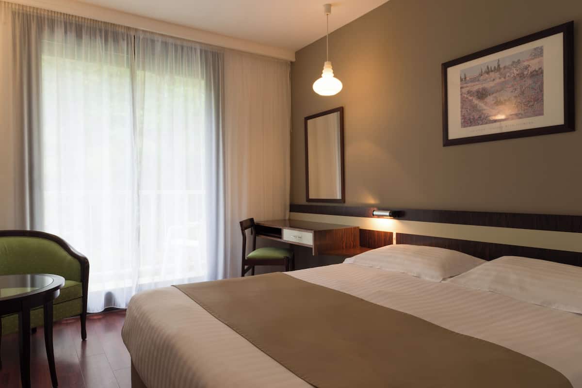 A hotel room with a bed, a desk, a chair, a lamp, and a window with curtains.