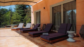 A sunlit outdoor seating area with lounge chairs and a tiled floor.