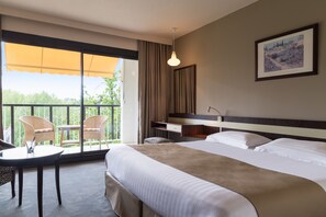 A hotel room with a large bed, a desk with chairs, a balcony with a view, and a framed picture on the wall. - Villa Borghese, The Originals Relais (Gréoux-les-Bains)