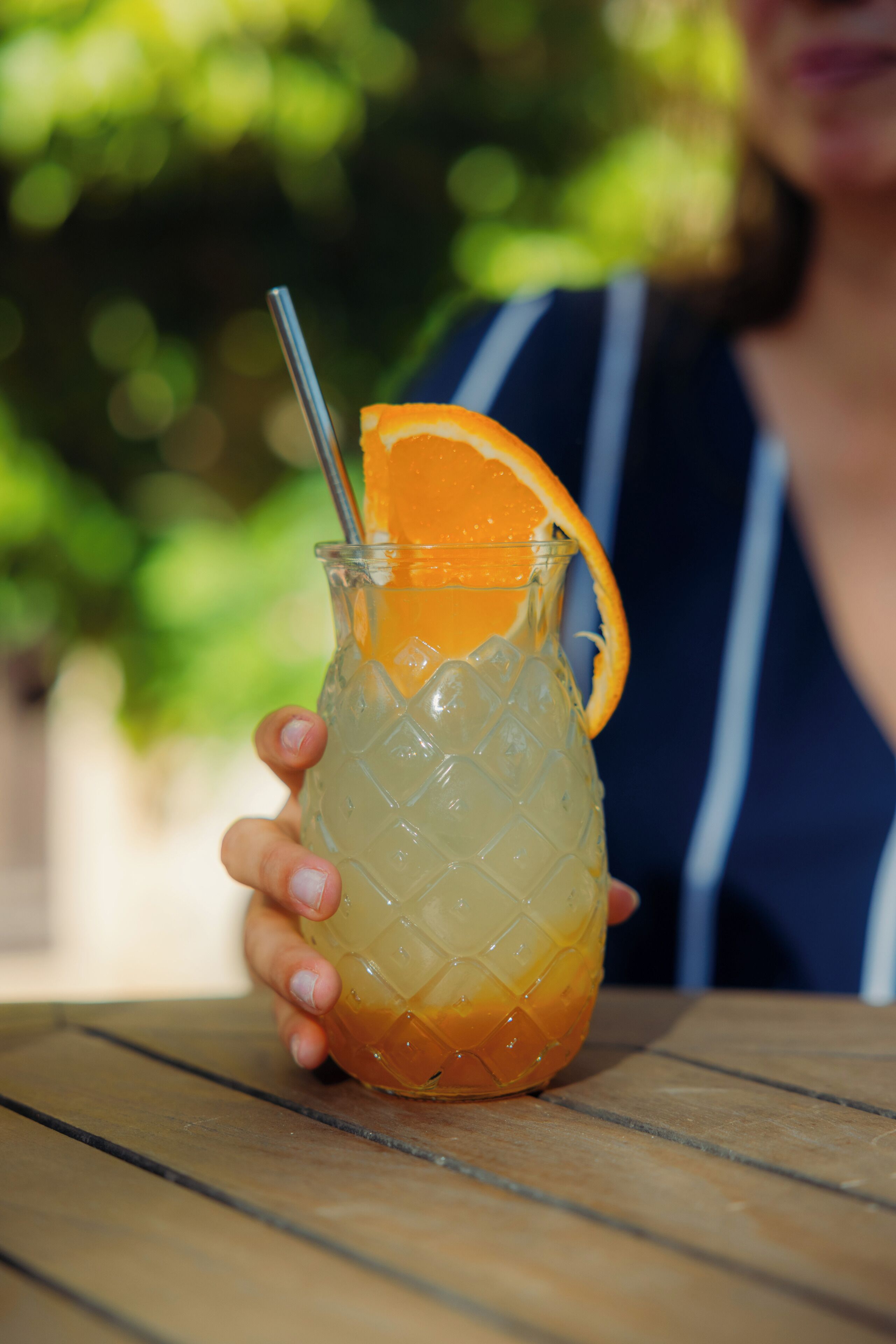 A person holding a glass with a straw, containing a beverage and an orange slice.