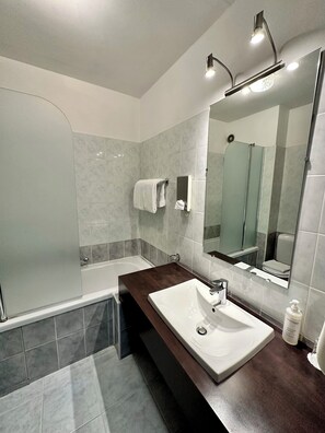 A modern bathroom with a large mirror, a bathtub, and a vanity with a sink. - Villa Borghese, The Originals Relais (Gréoux-les-Bains)