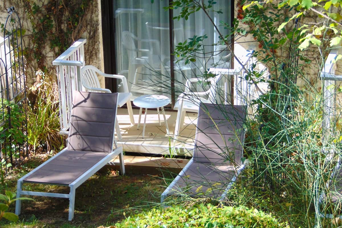 A patio with two lounge chairs, a small table, and a glass door leading to an indoor area with chairs.