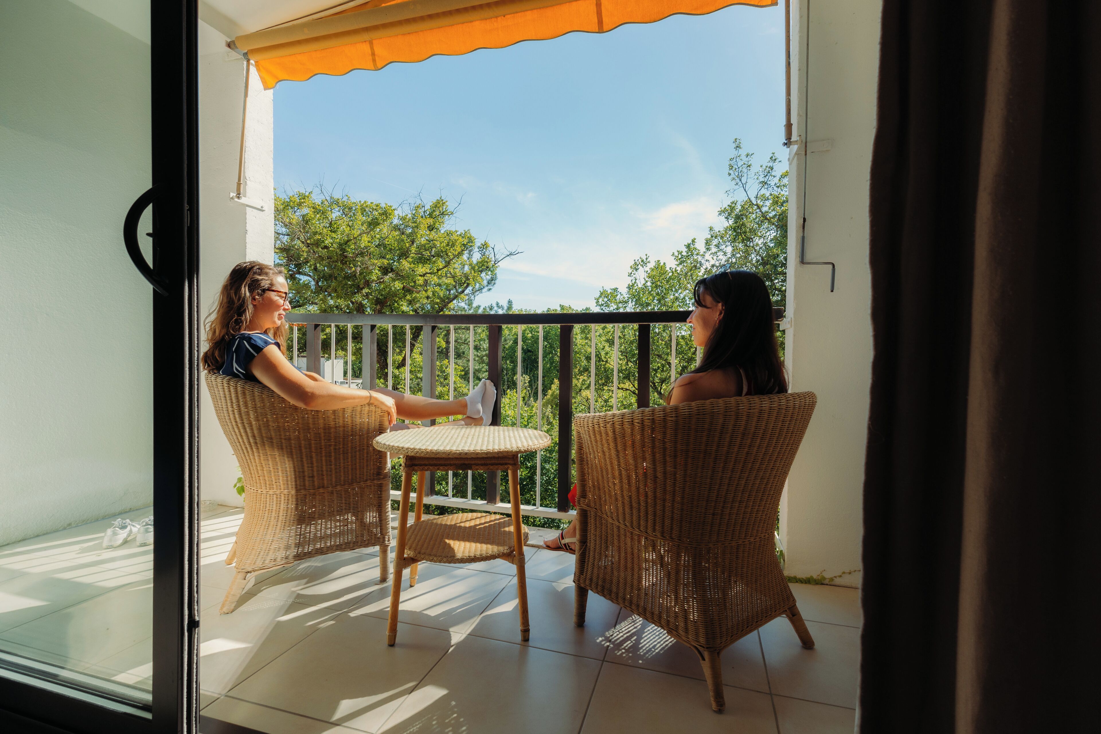Two wicker chairs facing each other on a balcony with a view of trees and a clear sky.