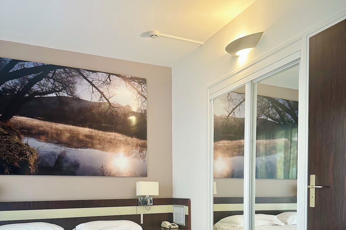 A hotel room with a large bed, a bedside table with a lamp, a phone, and a wall-mounted picture.