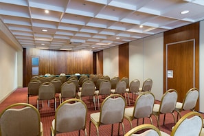Un salón de conferencias con filas de sillas, una mesa larga y un panel de pared de madera.
