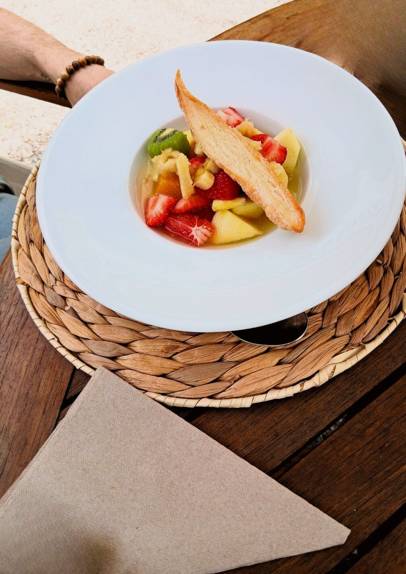 A white plate with a fruit salad and a piece of toast on a woven placemat.