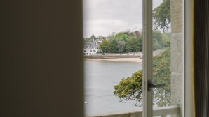 A view through a window with a white frame, overlooking a body of water, greenery, and buildings. - Villa Tri Men (Combrit)