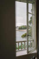 A view through a window with a white frame, overlooking a body of water, greenery, and buildings.