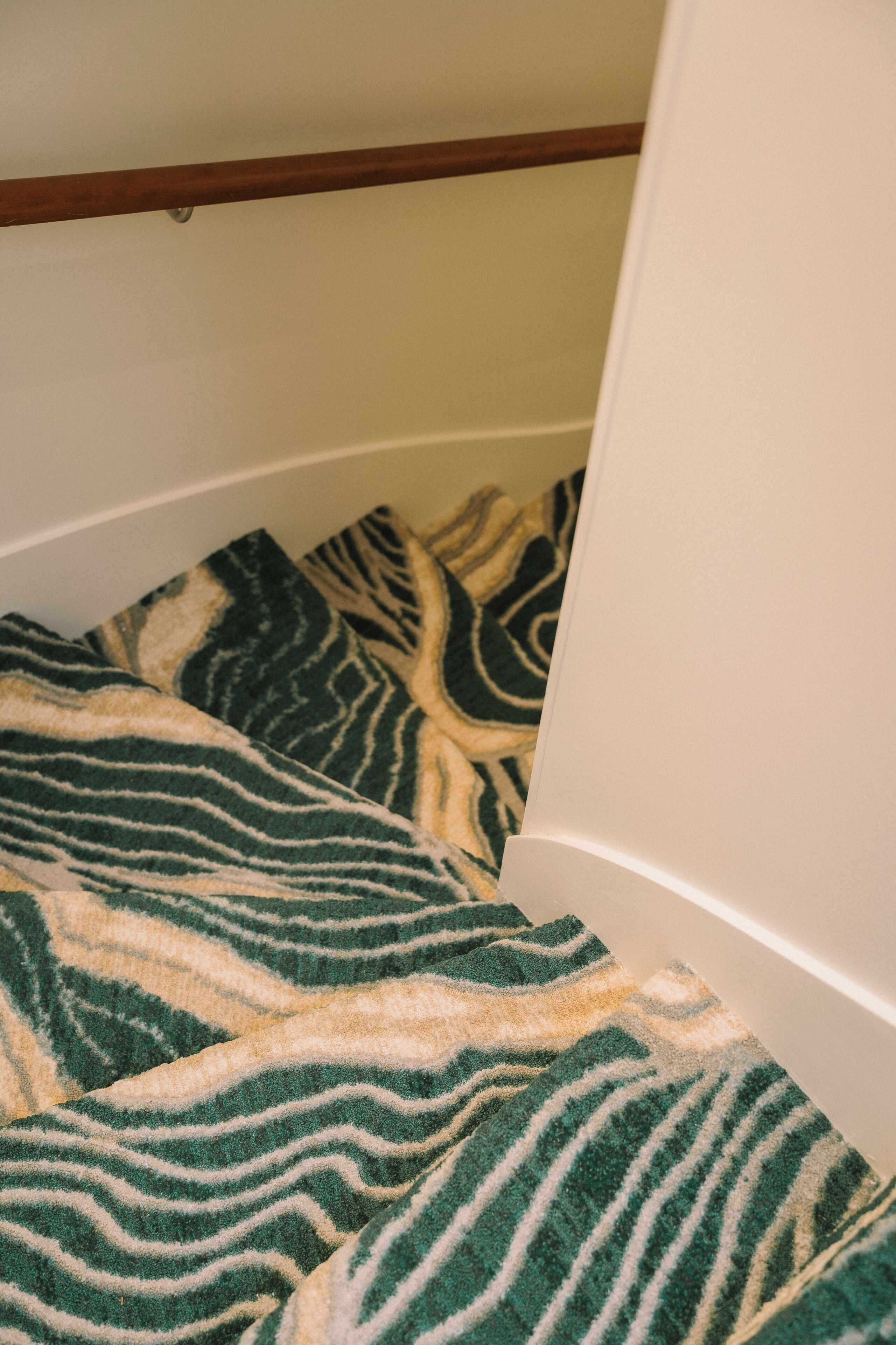 Una habitación con alfombra estampada, una viga de madera en el techo y una pared blanca.