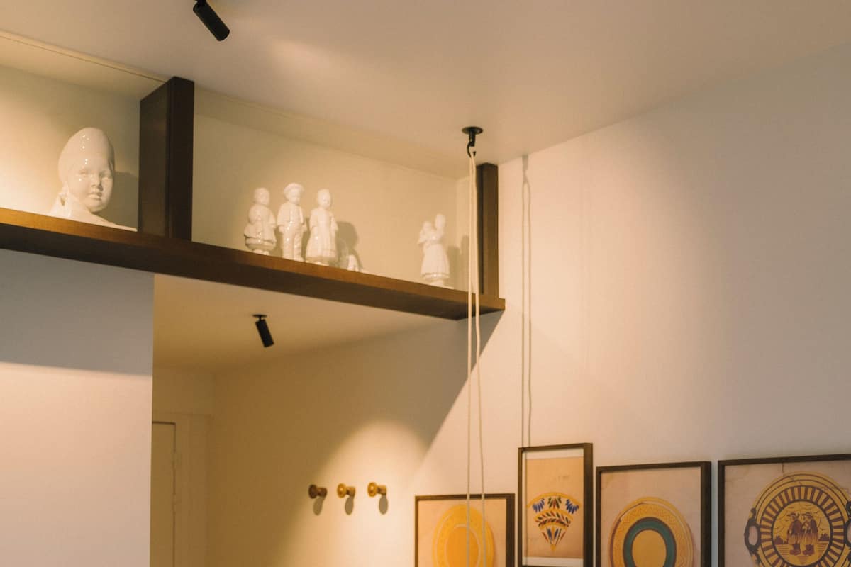 A bedroom with a bed, a nightstand, a shelf with busts, and wall-mounted artwork.
