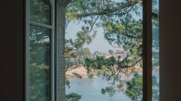 Une fenêtre donnant sur un lac, des arbres et une côte lointaine.