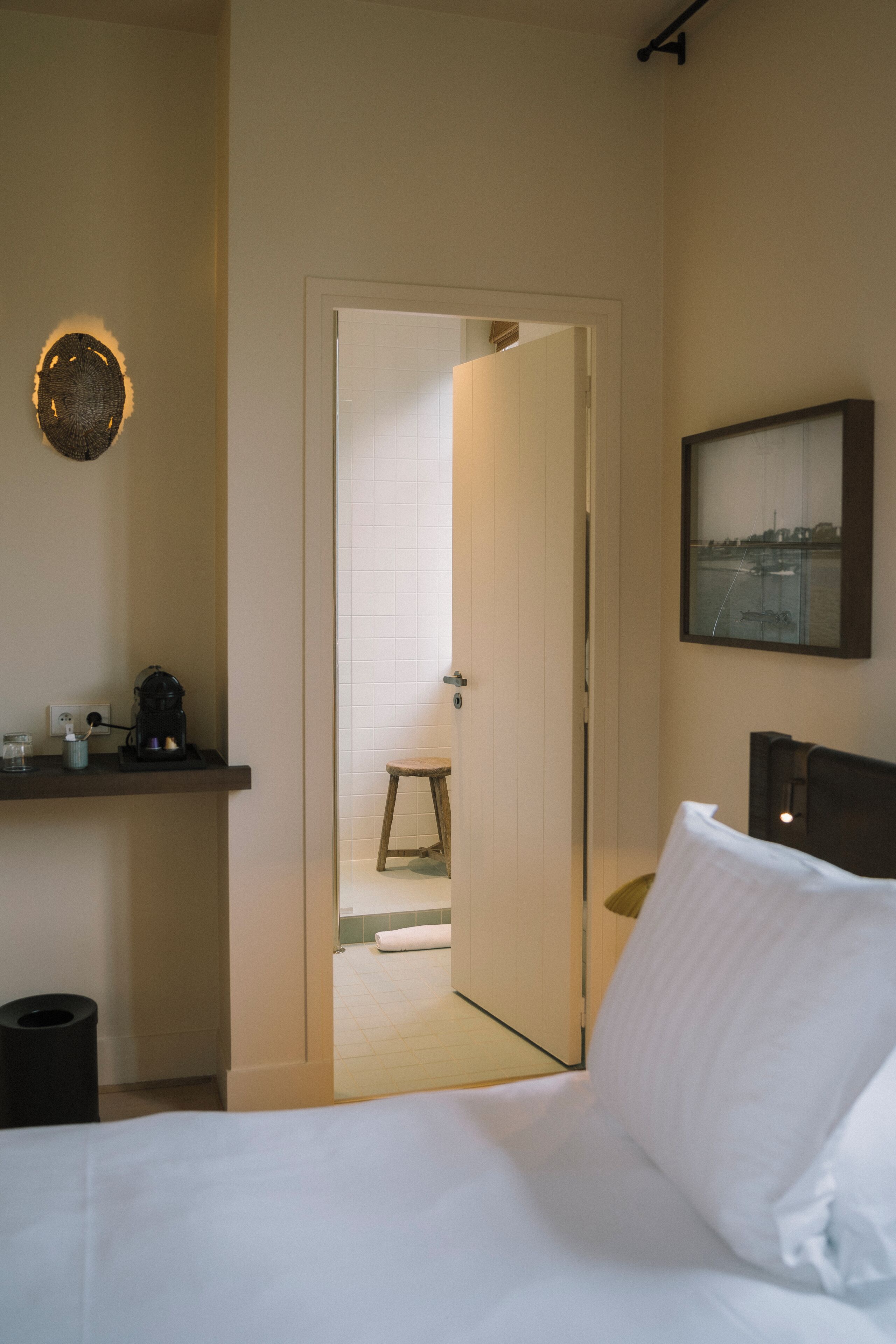 Habitación de hotel con cama, cafetera, un cuadro en la pared y una puerta que da al baño.