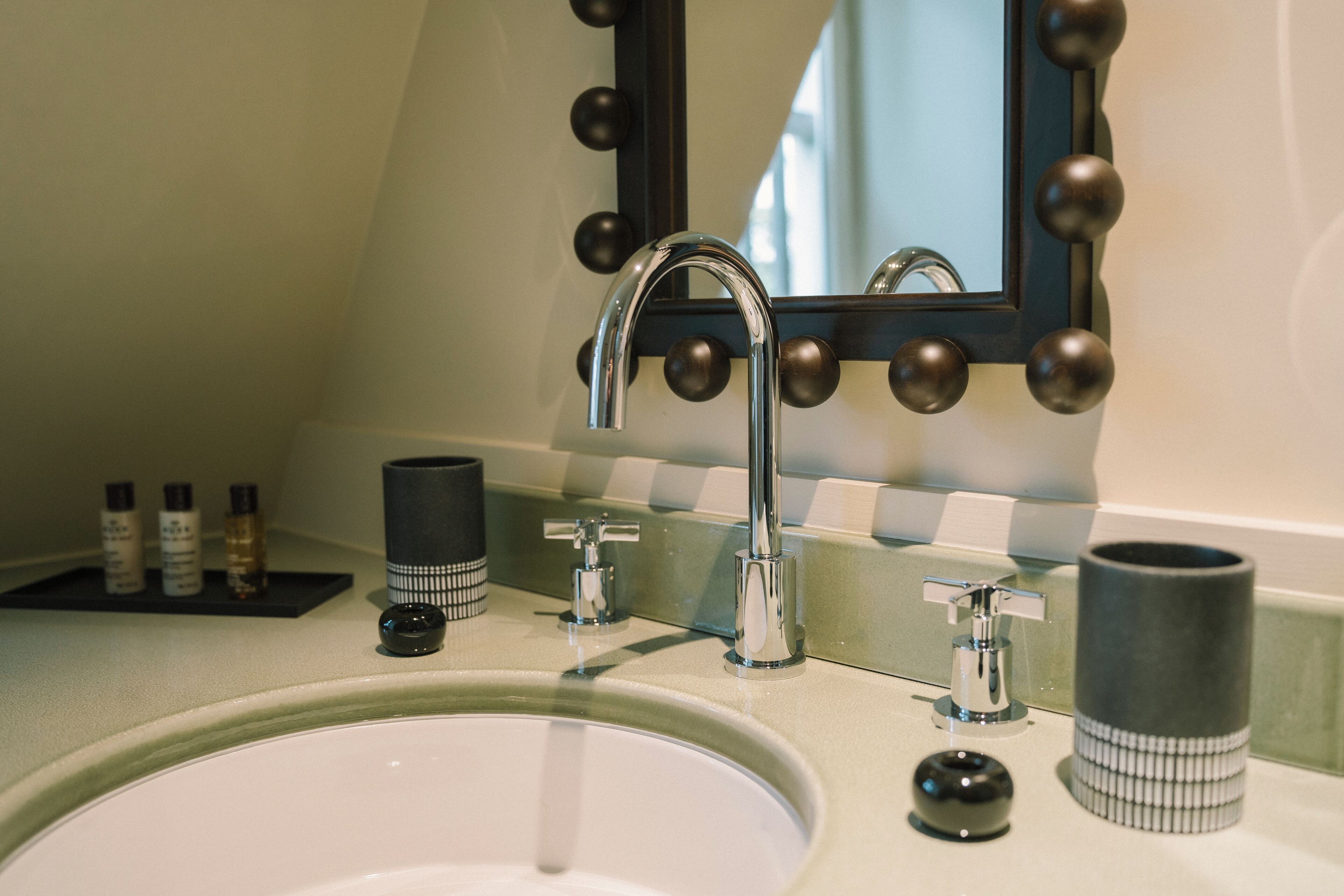 A bathroom with a sink, two faucets, a mirror with decorative lights, and toiletries on the counter.