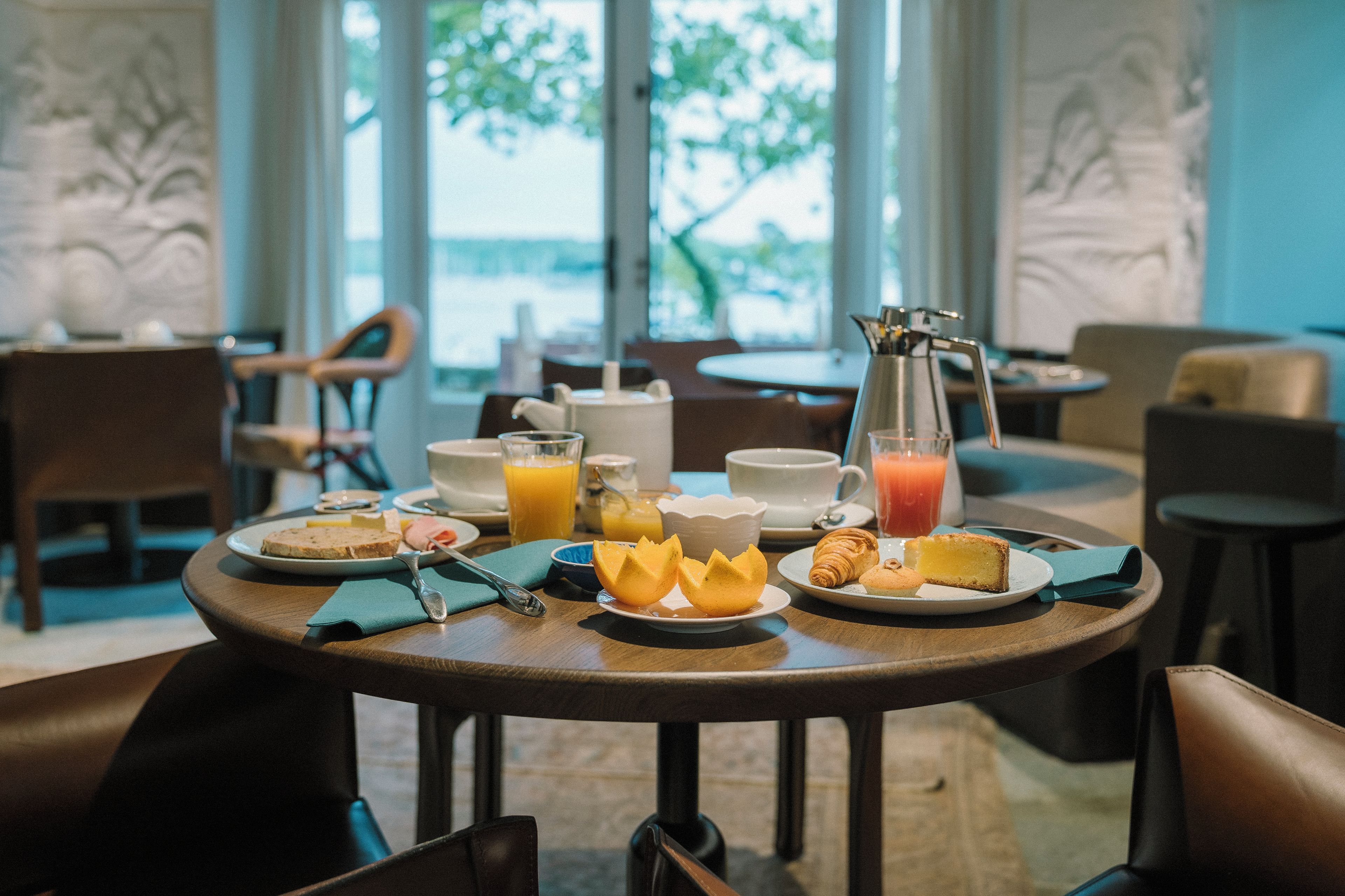 A breakfast setting with a table set for two, including plates with toast, fruit, and pastries, a pitcher of orange juice, and a coffee pot.