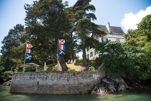 A stone wall with flags, a building with a sign reading "A TRI MEN", and a body of water.