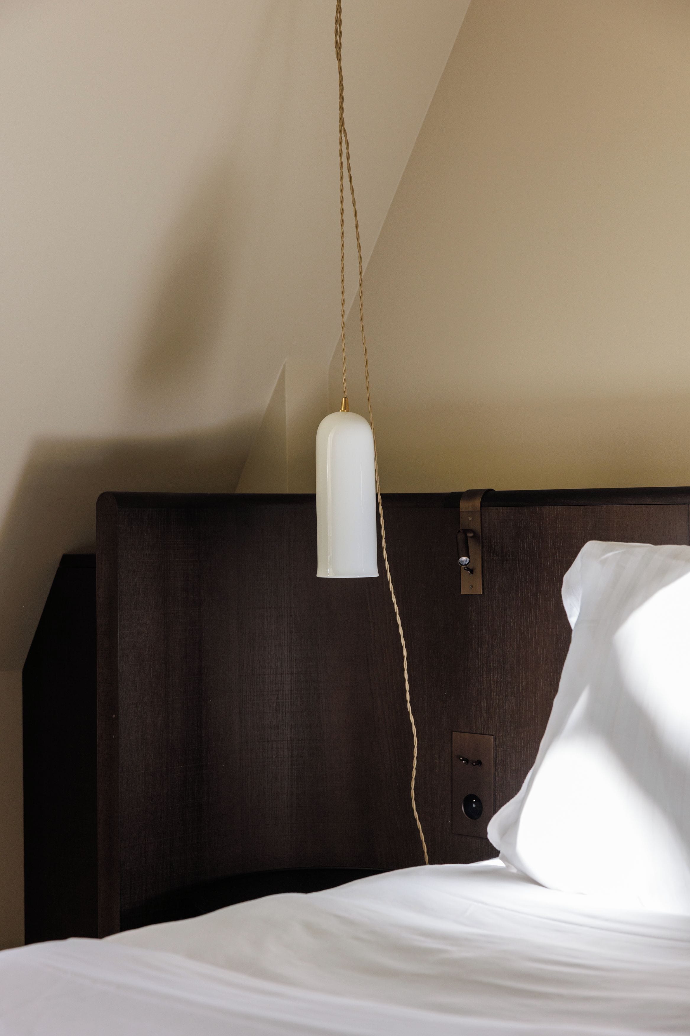 Un lit avec un oreiller blanc et une lampe suspendue.
