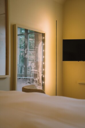 Une chambre d’hôtel équipée d’un lit, d’un téléviseur à écran plat fixé au mur et d’une fenêtre donnant sur une pièce avec un bureau et une chaise.